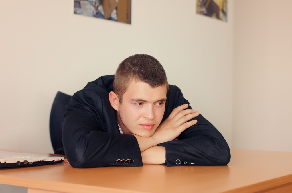 Young Businessman Resting Head on Desk and Looking Optimistic